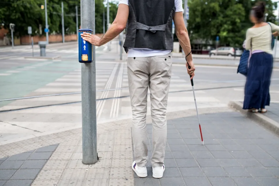 Pedestrian holding visual impairment cane pressing crosswalk button.